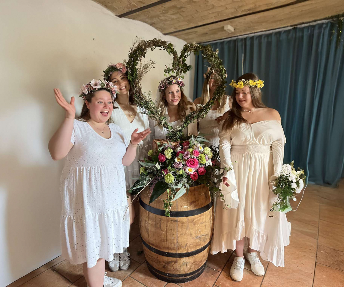 Frauen stehen am Fass mit Blumendeko drauf